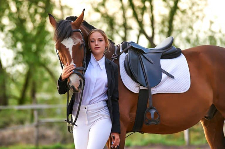 Young female equestrian model in riding attire standing with brown horse