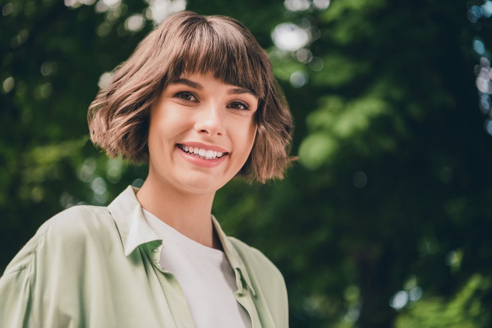 Young female model with short hair smiling outdoors in soft green shirt
