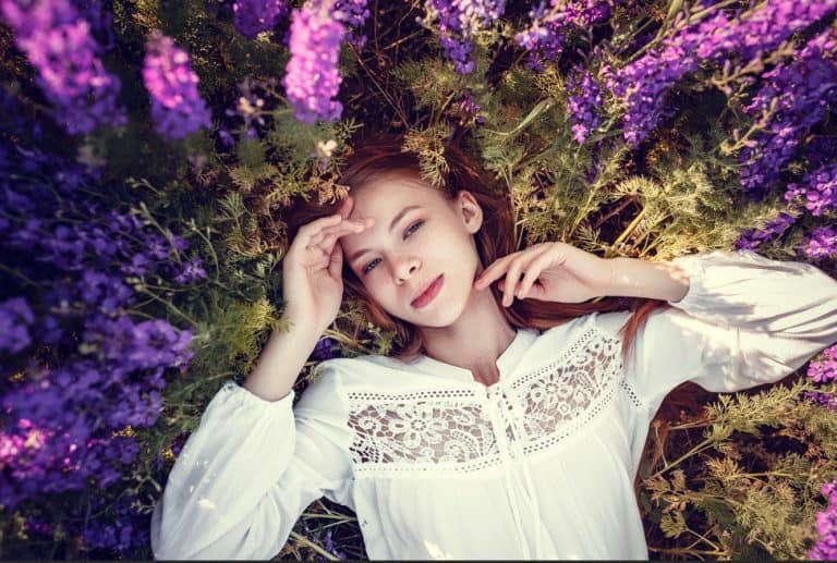 Female model lying in purple flowers, dreamy outdoor summer fashion shoot