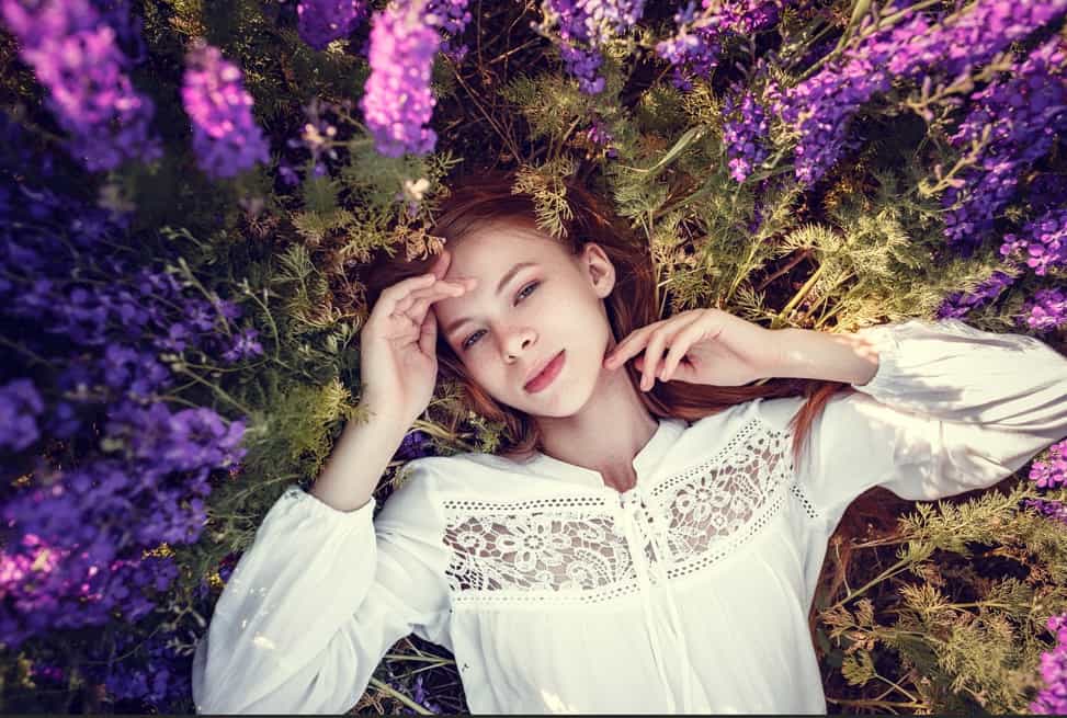 Female model lying in purple flowers, dreamy outdoor summer fashion shoot